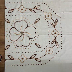 May include: White fabric with a floral design. The design features brown and tan dotted outlines of flowers and leaves. The flowers are in the center and along the top right corner of the fabric.