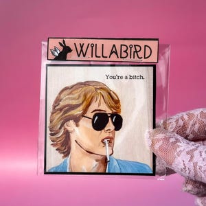 May include: An art print in a clear sleeve. The print shows a person wearing sunglasses and smoking a cigarette. The text "WILLABIRD" is at the top, with "You're a bitch." below the portrait.
