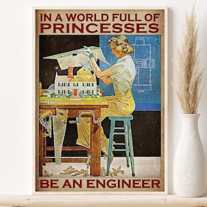 Puede incluir: Póster enmarcado de estilo vintage con el texto "IN A WORLD FULL OF PRINCESSES BE AN ENGINEER". La imagen muestra a una mujer trabajando en una maqueta de casa, con planos y herramientas. El póster está en una estantería de madera.