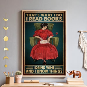 Puede incluir: Un póster enmarcado con el texto "THAT'S WHAT I DO I READ BOOKS I DRINK WINE AND I KNOW THINGS". La imagen presenta a una mujer con un vestido rojo sentada en una silla de mimbre, leyendo un libro con una copa de vino cerca. El fondo es turquesa.