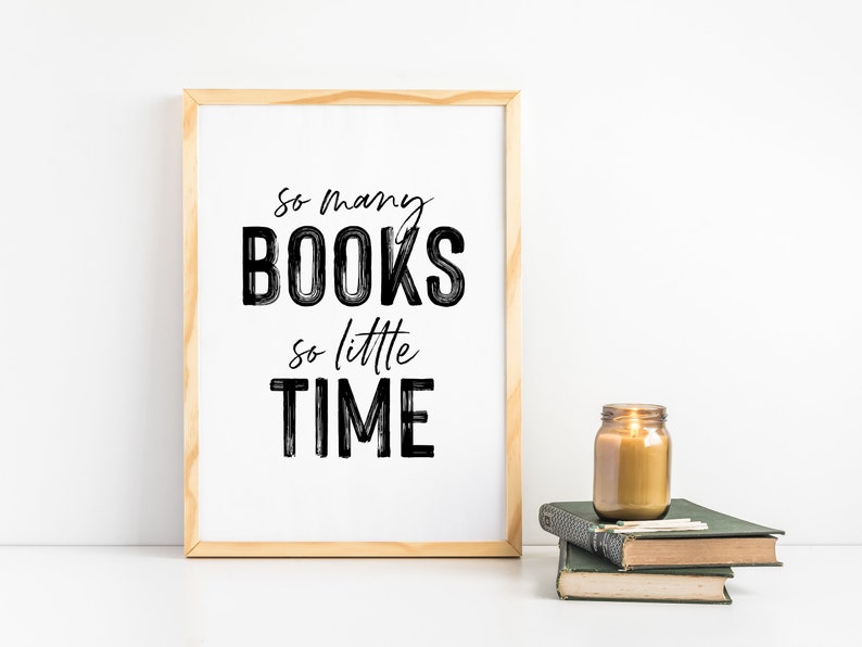 May include: A framed print with the text "So many BOOKS so little TIME" in black brush script on a white background. The print is sitting on a white surface next to a lit candle in a glass jar and a stack of books.