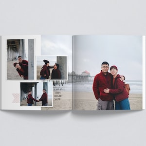 May include: A couple poses for a photo shoot on a beach. The man is wearing a red sweater and the woman is wearing a red jacket. They are standing in front of a pier and the ocean is in the background. The text "Loving this right now." is written on the page.