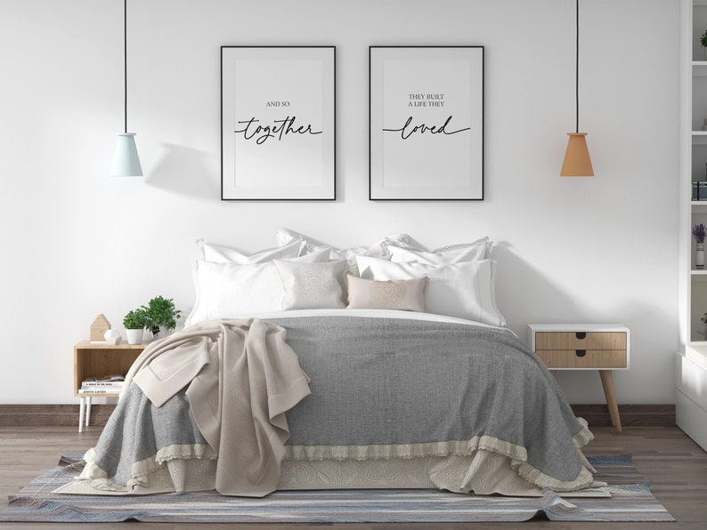 May include: A bedroom with a gray and white bed, two black framed prints with the text "And so together" and "They built a life they loved", a wooden nightstand with a lamp, and a rug on the floor.