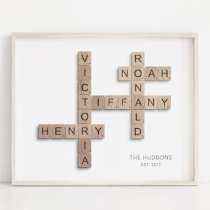 May include: A framed artwork featuring a scrabble tile crossword puzzle with the names "Henry", "Victoria", "Tiffany", "Noah", and "Ronald". The text "The Hudsons Est. 2013" is below the puzzle.