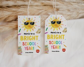 Op de afbeelding: Twee rechthoekige witte cadeaulabels met touwtje, voorzien van een gele zon met een zwarte zonnebril, schoolspullen zoals boeken, potloden en kleurpotloden, en de tekst Here's to a BRIGHT SCHOOL YEAR! From Olivia in kleurrijke letters.