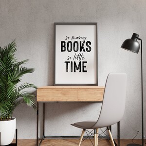 May include: A black framed print with the text "So many books, so little time" hanging on a gray wall above a wooden desk with a white chair and a black floor lamp.