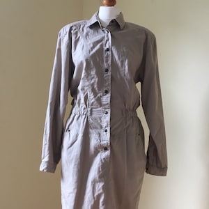 May include: A long-sleeved, light beige button-down dress with a cinched waist and pockets.