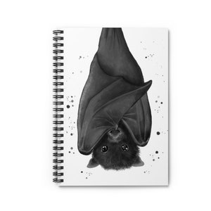 May include: A black and white illustration of a bat hanging upside down. The bat has large, round eyes and a small, pointed nose. The bat's wings are spread out and its body is curled up. The background is white with black splatters.