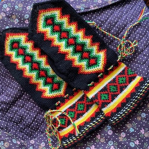 Puede incluir: Un par de manoplas de punto negro con un vibrante patrón geométrico en rojo, amarillo y verde. Los puños muestran un motivo de diamantes con cordones trenzados a juego en la misma paleta de colores para un ajuste seguro en las muñecas.