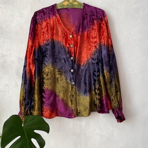 May include: A long-sleeved button-down shirt featuring a diagonal tie-dye pattern in shades of purple, red, and gold. The fabric has a velvet-like texture and includes vertical embroidered floral vine details along the front panels.