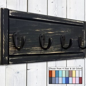 May include: A black wooden wall-mounted coat rack with four black metal hooks. The wood has a distressed finish, with visible grain and a slightly worn appearance. The image includes a color palette with options for sizes and colors.