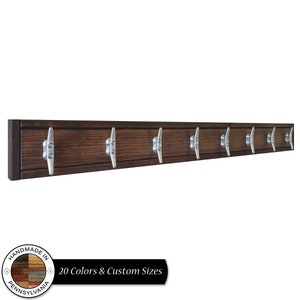 May include: A dark brown wooden wall mounted coat rack with eight silver metal boat cleat hooks. The rack is handmade in Pennsylvania. The text "20 Colors & Custom Sizes" is below the rack.
