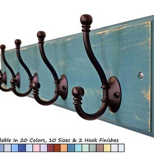 May include: A rustic wall-mounted coat rack with six dark bronze hooks. The hooks are mounted on a distressed teal-colored wooden board. The text at the bottom says "Available In 20 Colors, 10 Sizes & 2 Hook Finishes."