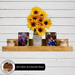 May include: A rustic wooden shelf with two candles, two framed photos, and a mason jar filled with sunflowers. The shelf is mounted on a white wood wall. The text "HANDMADE IN PENNSYLVANIA" and "20 Colors & Custom Sizes" is visible below the shelf.