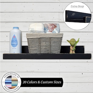 May include: Black wooden shelf with a gray wicker basket, a bottle of baby powder, and a small green figurine. The shelf is mounted on a white wood wall. The text "Extra Deep" is visible in a circle above the shelf. The text "Handmade in Pennsylvania" is visible in a circle below the shelf. The text "20 Colors & Custom Sizes" is visible below the shelf.