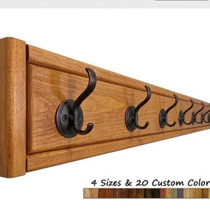 May include: A wooden coat rack with multiple dark bronze hooks. The rack is made of stained wood and features a rectangular design. The text "4 Sizes & 20 Custom Colors" is displayed below the rack.