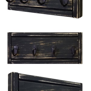 May include: A black wooden wall-mounted coat rack with five black metal hooks. The wood has a distressed finish with visible grain and light-colored accents. The hooks are attached with screws.