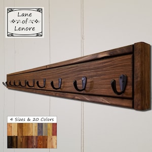 May include: A wooden coat rack with six black metal hooks. The rack is stained a dark brown color and has a simple, rustic design. The text "Lane of Lenore" is visible in a small frame above the rack. The text "4 Sizes & 20 Colors" is visible below the rack, along with a sample of different wood colors.
