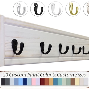 May include: White wooden wall mounted coat rack with five black metal hooks. The rack has a distressed white finish and is 20 inches long. The hooks are 2 inches long and have a rounded shape. The rack is shown with a sign that says "20 Custom Paint Color & Custom Sizes" and a color chart of 20 different paint colors.