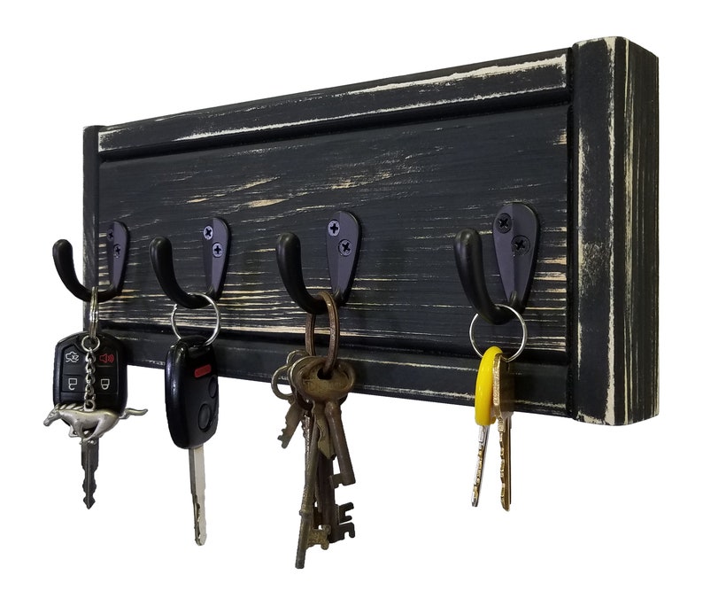 May include: A black wooden key holder with four metal hooks. The wood has a distressed finish with visible grain and white accents. Various keys and key fobs hang from the hooks, showcasing a practical and rustic design.