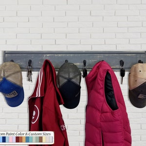 May include: A rustic wooden coat rack with six hooks, painted in a distressed gray finish. The rack is mounted on a white brick wall and has a variety of items hanging from it, including hats, jackets, and keys. The text "20 Custom Paint Color & Custom Sizes" is displayed below the rack, along with a color palette of 20 different paint colors.