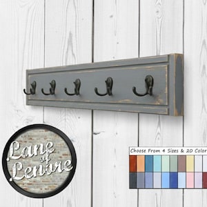 May include: A gray wooden coat rack with five black metal hooks. The rack is mounted on a white wooden wall. The image includes a logo that says "Lane of Lenore" and a color chart.