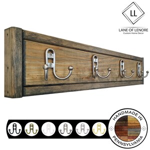 May include: Rustic wooden coat rack with five silver hooks. The rack is made of reclaimed wood and has a distressed finish. The hooks are made of metal and have a brushed nickel finish. The rack is labeled "Lane of Lenore Custom Home Decor" and "Handmade in Pennsylvania".