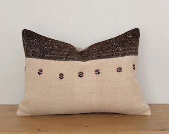 May include: A white pillow with a brown and black stripe across the center. The pillow has a small pattern of red and black diamonds along the center stripe.