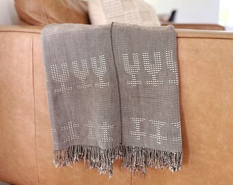 May include: A gray throw blanket with white fringe and the words "Love You" woven into the fabric. The blanket is draped over a brown leather couch.