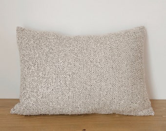 May include: A soft, off-white throw pillow with a textured woven fabric. The pillow is rectangular and has a subtle sheen.