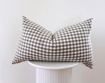 May include: A brown and white gingham pillow on a white pedestal.