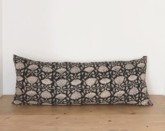 May include: A long black and white patterned pillow with a floral design. The pillow is on a wooden surface.