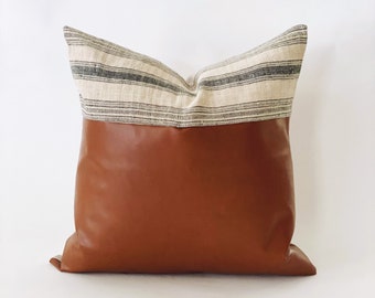 May include: A brown leather pillow with a white and gray striped fabric panel on the top.