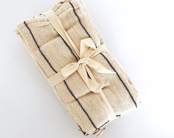 May include: A stack of beige kitchen towels with black stripes, tied together with a beige ribbon.