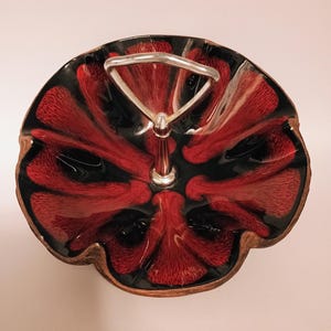 May include: A vintage serving dish with a red and black floral design. The dish has a silver handle and a brown rim. The interior features a glossy, textured pattern. A decorative piece for serving snacks or displaying items.