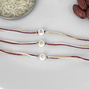 Rakhi con inicial dorada / Rakhi burdeos, dorado y blanco con cuentas con acento de letra / Rakhi para hermano, hilo Raksha Bandhan / Pulsera con letras personalizada