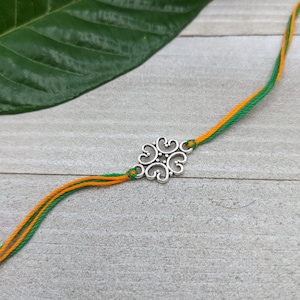 May include: A silver charm bracelet with a decorative, ornate charm in the centre. The bracelet is made of two strands of string, one green and one orange.