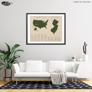 May include: A framed map of the United States with green markings showing the locations of national and state parks. The map is on a beige background with a list of park names below. The map is hanging on a white wall above a white couch.