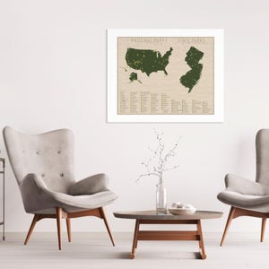 May include: A framed map of the United States with all the national parks and state parks highlighted in green. The map is on a beige background with a white frame. The map is hanging on a white wall in a living room setting with two armchairs and a coffee table.
