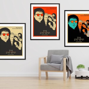 Puede incluir: Tres carteles de cine enmarcados para la pel&iacute;cula "The Lost Boys". Cada cartel presenta un grupo diferente de personajes de la pel&iacute;cula, incluyendo un vampiro con gafas de sol rojas y un vampiro con gafas de sol azules. Los carteles est&aacute;n colocados contra una pared blanca con un sill&oacute;n gris y dos mesas auxiliares.