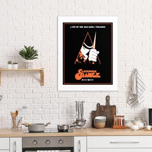 May include: A black and white poster with a red and orange title that reads "Clockwork Orange". The poster features a man in a white shirt and black hat holding a knife.