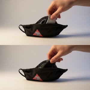 May include: Black face mask with a black and white patterned interior. A white filter is being inserted into the mask. The mask has a red triangle logo on the front. The mask has two handles.