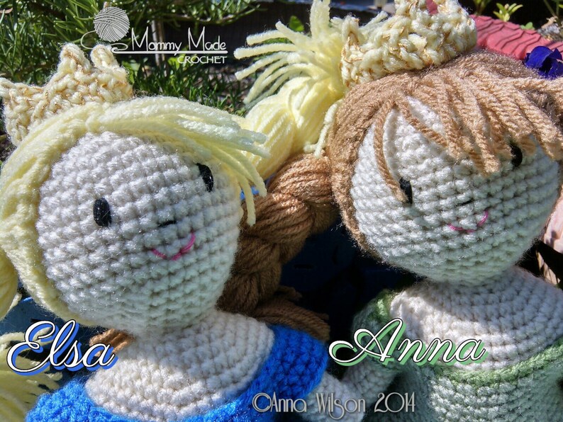 May include: Two crocheted dolls, Elsa and Anna, from the movie Frozen, wearing crowns and dresses. The dolls are made with white yarn and have black eyes and pink lips. The dolls are sitting on a green surface.