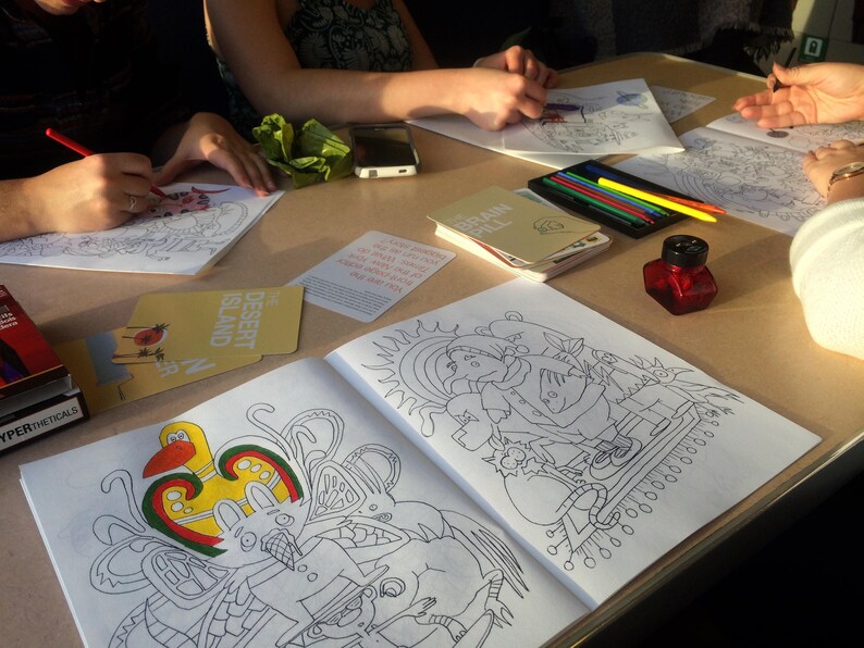 May include: A table with several coloring books and coloring supplies. The coloring books have black and white illustrations of people, animals, and objects. The coloring supplies include colored pencils, markers, and a bottle of ink.