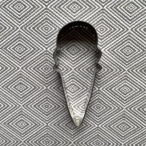 May include: A metal cookie cutter shaped like an ice cream cone. The cutter is silver and has a smooth surface.
