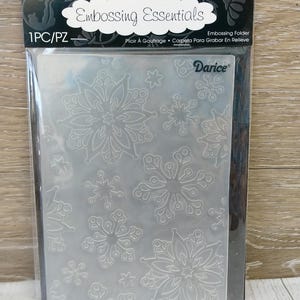 May include: A clear embossing folder with a snowflake design. The package reads "Embossing Essentials" and "Darice". The folder is designed for creating embossed patterns on paper or cardstock for crafts and scrapbooking.