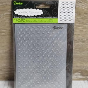 May include: A clear, plastic embossing folder with a dotted pattern. The package includes the text "Embossing Essentials" and measurements of 4.25 inches by 5.75 inches. The brand name "Darice" is visible on the package.