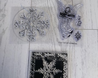 May include: Clear stamps featuring winter and holiday designs. Includes a large snowflake, an angel holding a book with the word "Rejoice", and a snowflake with the words "Winter Wonderland".