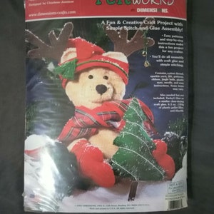 May include: A Feltworks craft kit featuring a teddy bear wearing a red hat, scarf, and boots, holding a green felt Christmas tree. The kit is approximately 13 inches (33 cm) tall and includes patterns, felt, and instructions for simple stitching and glue assembly.