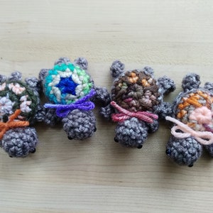 May include: Four crocheted turtle figurines with different colored shells. The turtles are gray with black eyes and have a small bow tied around their necks.